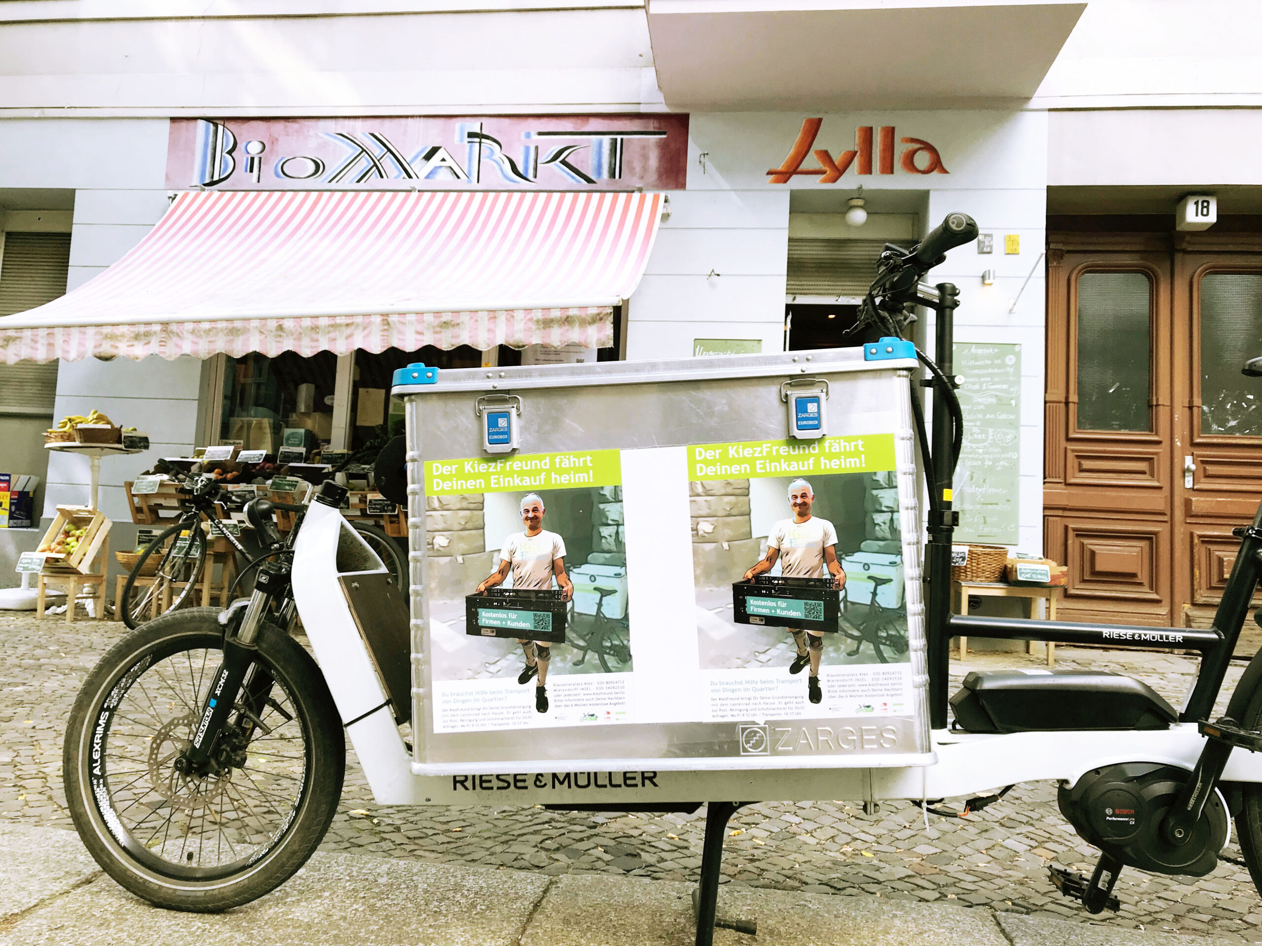 Ein Lastenrad steht vor einem Biomarkt, auf der Lastenradbox sind zwei Plakate vom KiezFreund befestigt.