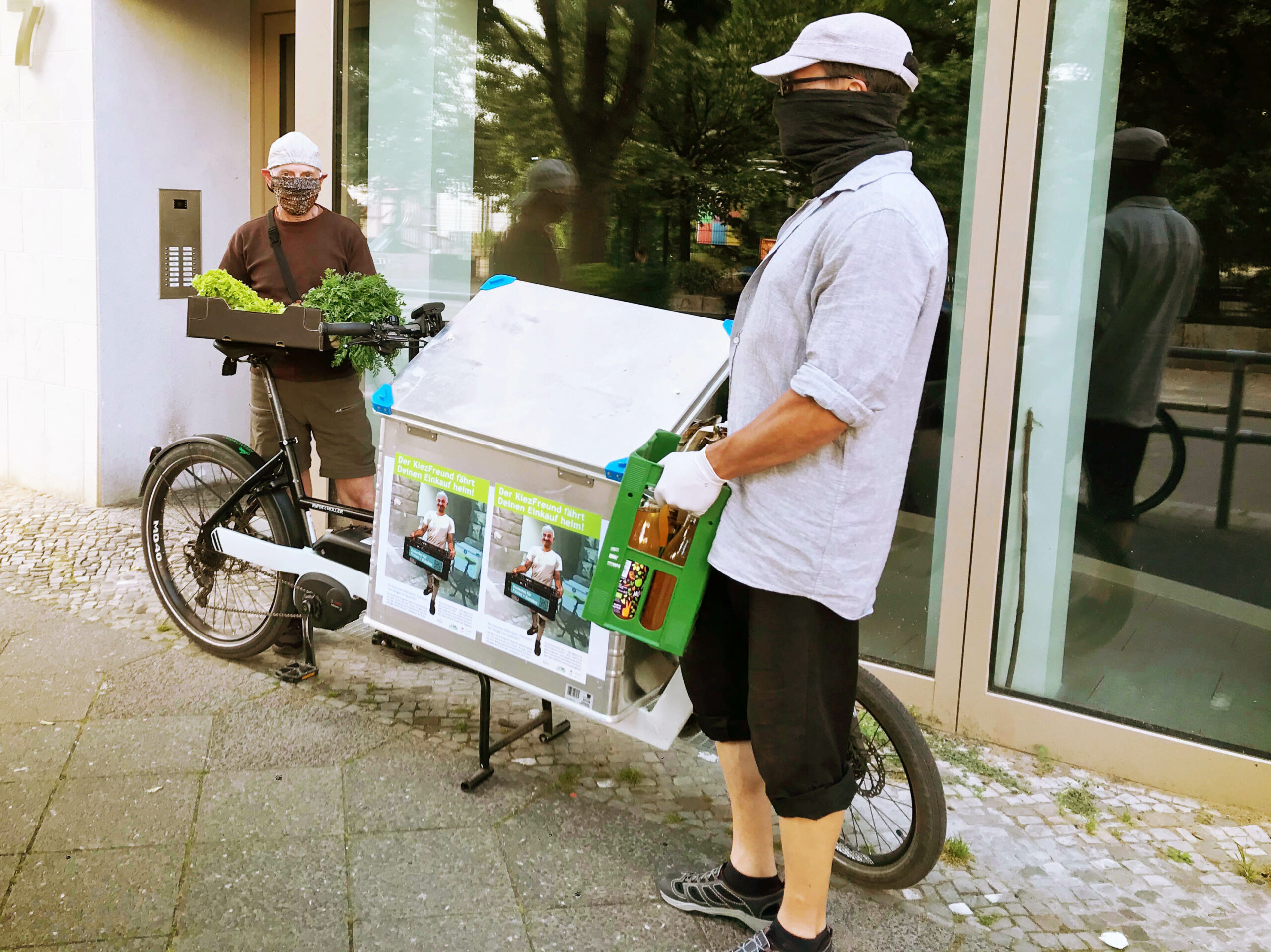 Zwei Personen liefern mit einem Lastenrad Gemüse und eine Kiste Saft aus.