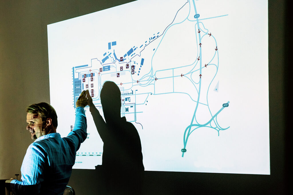 Eine Person zeigt auf eine Präsentationsfolie, die auf eine Wand projiziert wird.